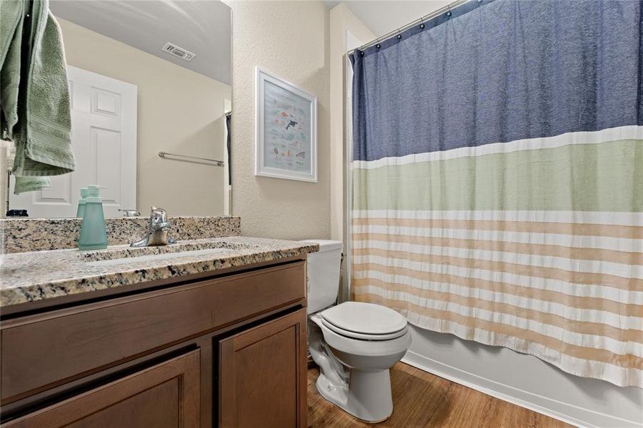 Full bath with shower / bath combination with curtain, dark wood-type flooring, a textured wall, and vanity