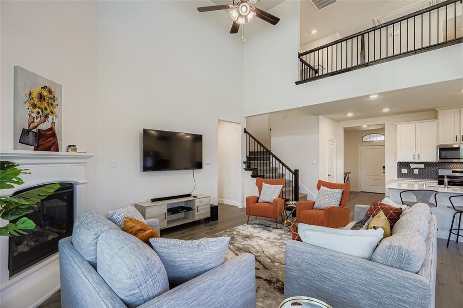 Living area featuring a glass covered fireplace, wood finished floors, stairs, a towering ceiling, and ceiling fan