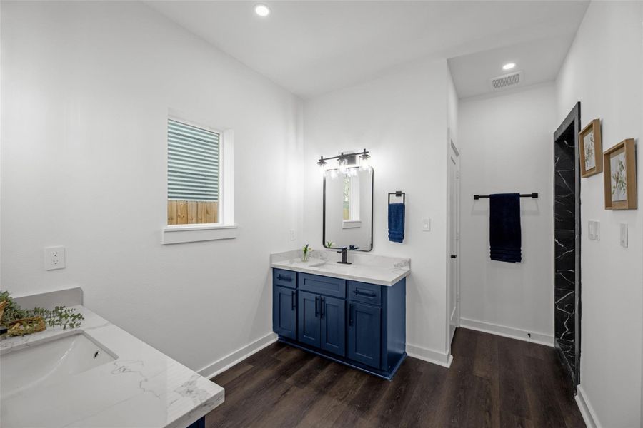 Stylish blue vanity with dual sinks and a large mirror, complemented by elegant lighting. The room is well-lit with natural light from a small window, and there's a spacious walk-in shower visible in the background. Stylish blue vanity with dual sinks and a large mirror, complemented by elegant lighting. The room is well-lit with natural light from a small window, and there's a spacious walk-in shower visible in the background.