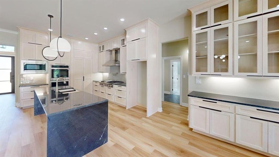 Kitchen featuring a sink, appliances with stainless steel finishes, wall chimney exhaust hood, glass insert cabinets, and a center island with sink