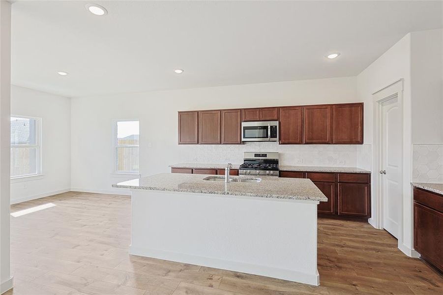 Kitchen with light stone countertops, appliances with stainless steel finishes, light wood-type flooring, and a center island with sink