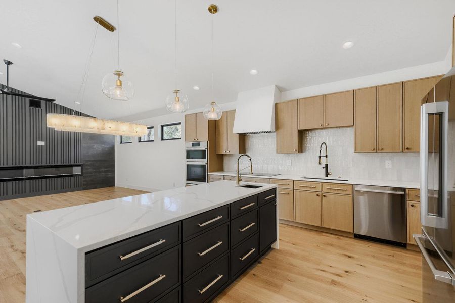 Kitchen with light stone counters, light wood-style floors, a spacious island, stainless steel appliances, and hanging light fixtures Kitchen with light stone counters, light wood-style floors, a spacious island, stainless steel appliances, and hanging light fixtures