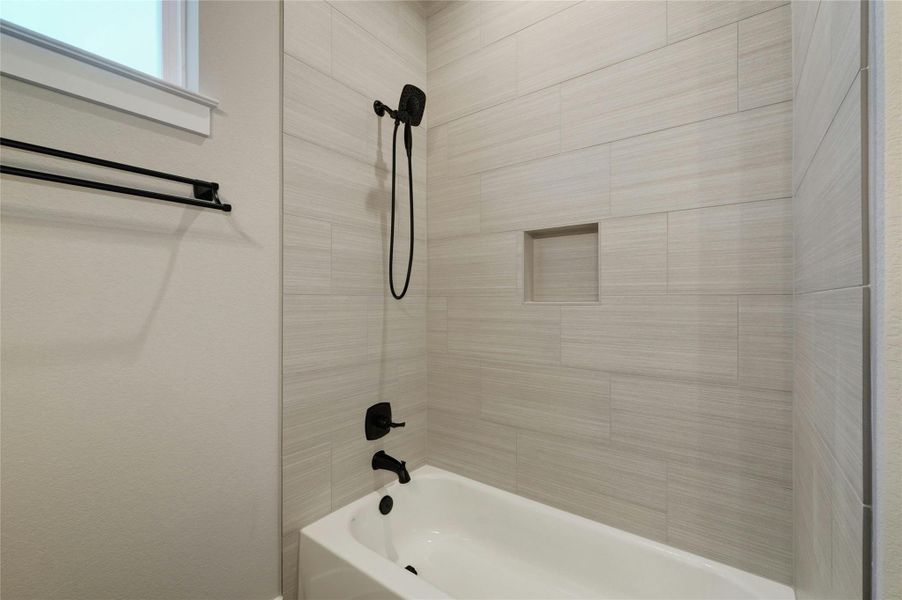 Bathtub and shower combination featuring floor-to-ceiling rectangular wall tiles, a built-in shower niche, and matte black fixtures