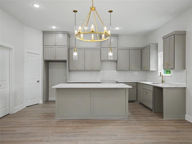 Modern kitchen featuring a central island with a white countertop, extensive grey cabinetry, light wood-finish flooring, a white subway tile backsplash, and recessed ceiling lights