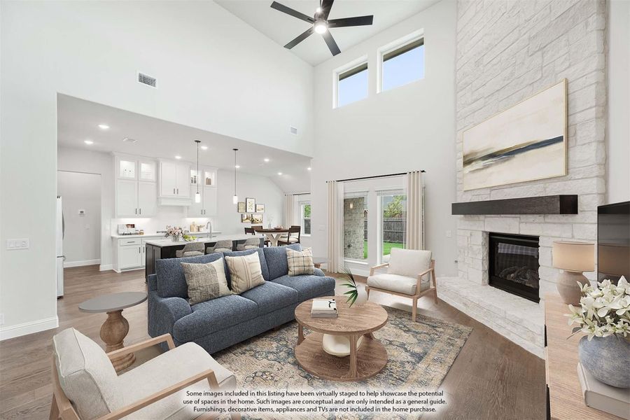 Open-concept living room with vaulted ceiling, stone fireplace, and view into white kitchen with hardwood floors Open-concept living room with vaulted ceiling, stone fireplace, and view into white kitchen with hardwood floors