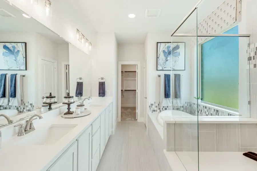 Master bathroom with double vanity, soaking tub, glass shower, and walk-in closet access