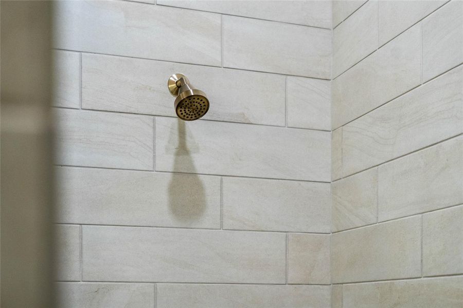 The fixed shower head and arm assembly feature a warm-toned, metallic finish. This finish adds a luxurious, modern accent that contrasts beautifully with the cool-toned tiles.