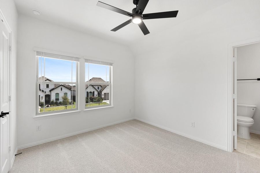 Empty bedroom with carpet, ceiling fan, two windows, and an attached bathroom doorway Empty bedroom with carpet, ceiling fan, two windows, and an attached bathroom doorway