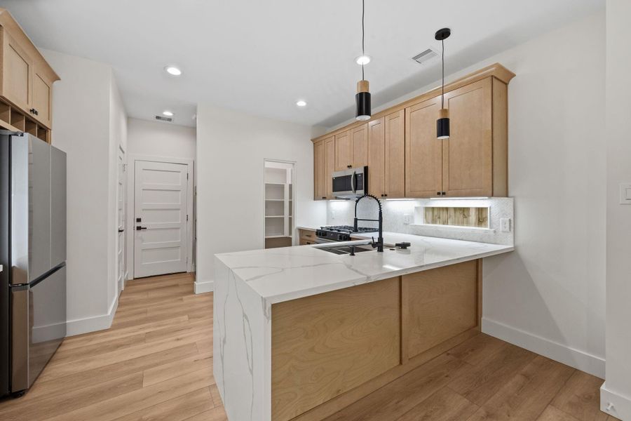 Modern kitchen with sleek stainless steel appliances, light wood cabinetry, and elegant pendant lighting over a spacious marble island.
