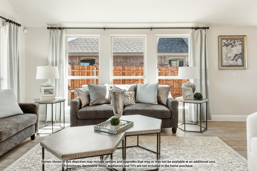 Living room with gray sofa, geometric coffee table, area rug, and three large windows with curtains Living room with gray sofa, geometric coffee table, area rug, and three large windows with curtains