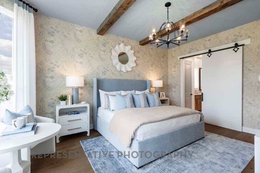 Bedroom featuring wallpapered walls, wood finished floors, beam ceiling, a chandelier, and a barn door