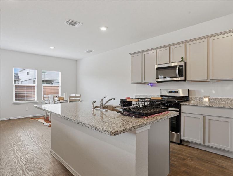 Smooth wood flooring runs under classic cabinetry and a central stone island. Smooth wood flooring runs under classic cabinetry and a central stone island.