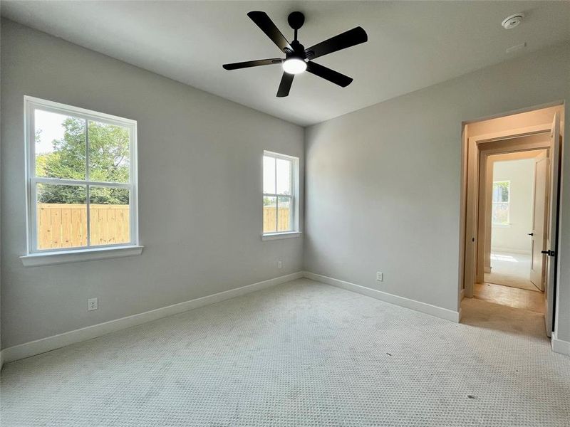 Empty room featuring ceiling fan, light carpet, and plenty of natural light