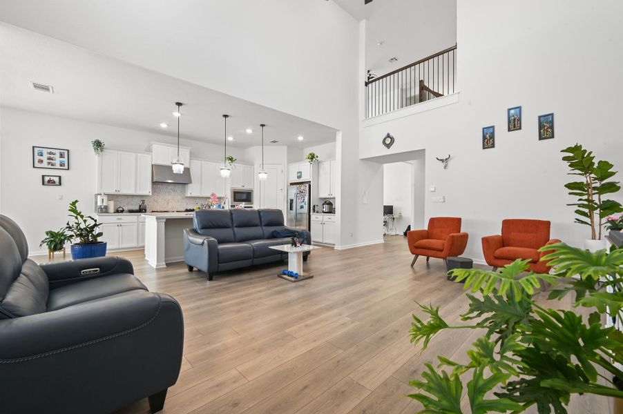 Double-height ceilings and rich wood-style flooring anchor this open-concept main living space.