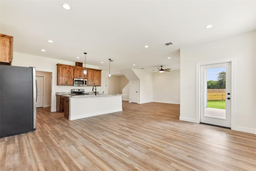 Kitchen with light wood look floors, stainless steel appliances, ceiling fan, and a center island with sink Kitchen with light wood look floors, stainless steel appliances, ceiling fan, and a center island with sink