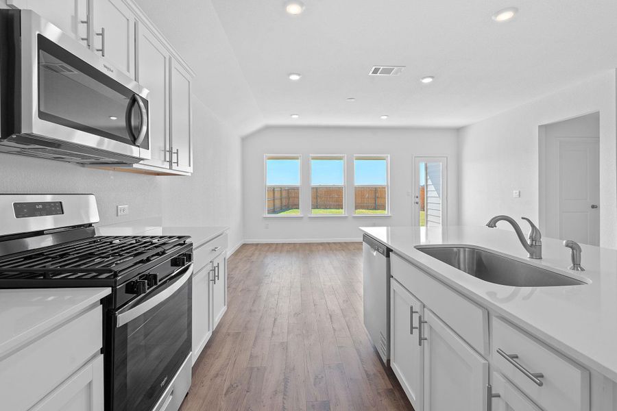 Kitchen with appliances with stainless steel finishes, white cabinetry, dark wood-type flooring, light stone counters, and recessed lighting