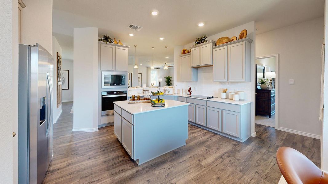 Kitchen with stainless steel appliances, a kitchen island, dark wood finished floors, light stone countertops, and decorative light fixtures Kitchen with stainless steel appliances, a kitchen island, dark wood finished floors, light stone countertops, and decorative light fixtures