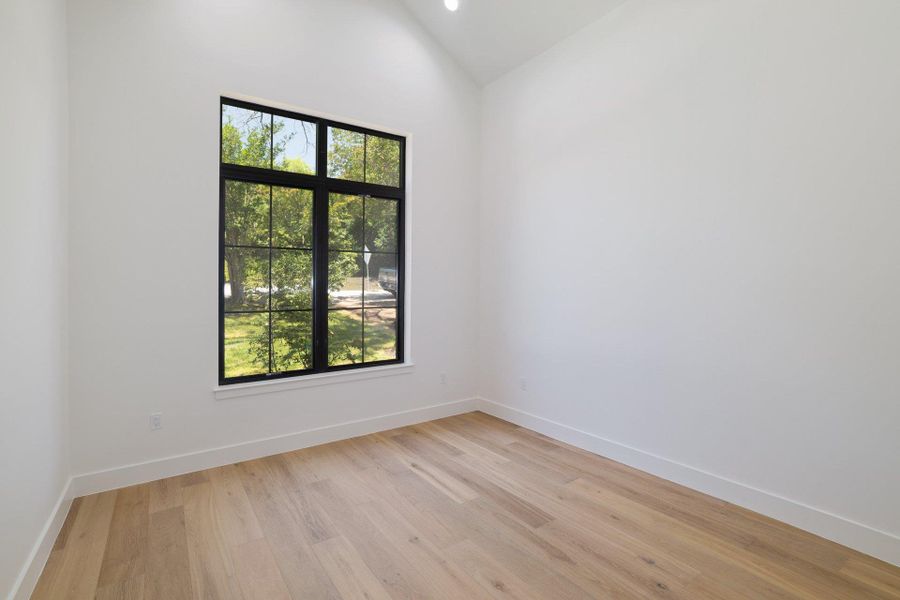 Room featuring a large black-framed window with grid panes, wood-finish flooring, and crisp white walls
