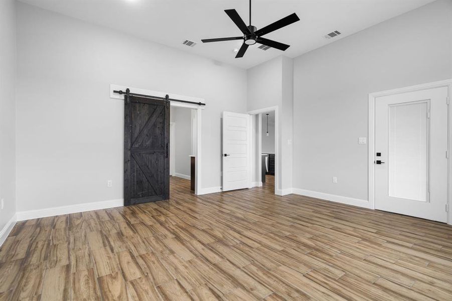 Unfurnished bedroom featuring ceiling fan, a barn door, a towering ceiling, and light hardwood / wood-style flooring