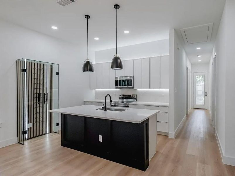 Kitchen featuring light wood finished floors, appliances with stainless steel finishes, an island with sink, white cabinetry, and recessed lighting