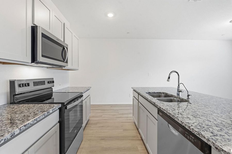 Modern kitchen featuring light cabinetry, stainless steel appliances, speckled stone countertops, and wood-finish flooring Modern kitchen featuring light cabinetry, stainless steel appliances, speckled stone countertops, and wood-finish flooring