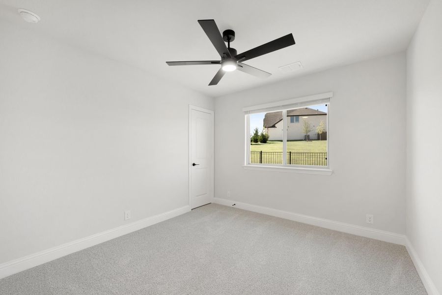 Empty bedroom with gray carpet, white walls, black ceiling fan, and single window with backyard view