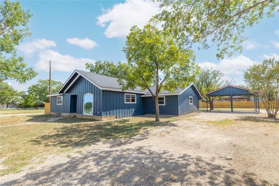 View of front of property with board and batten siding, dirt driveway, a detached carport, and a shingled roof View of front of property with board and batten siding, dirt driveway, a detached carport, and a shingled roof