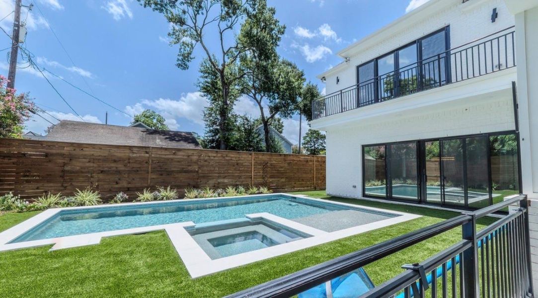 This modern home features a spacious backyard with a sleek pool and spa, surrounded by lush greenery and a wooden privacy fence. Large glass doors and windows provide ample natural light and a seamless indoor-outdoor flow.