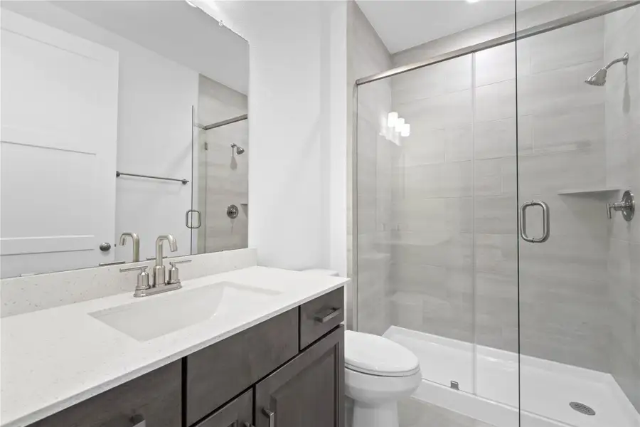 The ensuite secondary bathroom features a framed and spacious walk-in shower with tile surround, tile flooring,  vanity with a stunning light countertop, a stylish mirror, sleek fixtures, and contemporary finishes throughout.