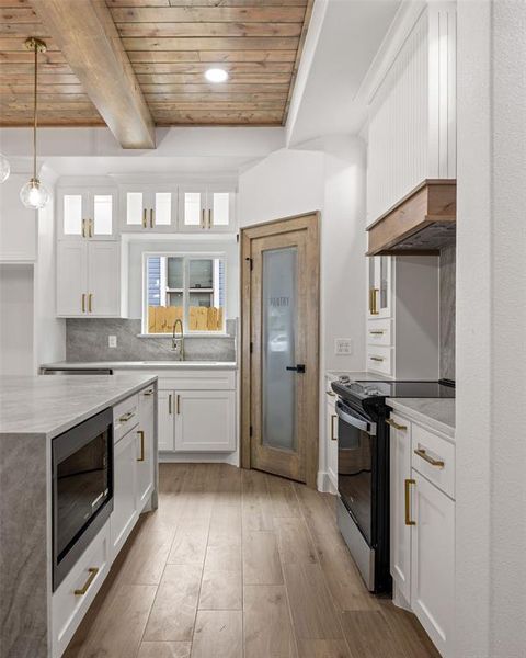 Contemporary kitchen featuring white cabinetry with gold-finish hardware, wood-finish flooring, and a wood-paneled ceiling with exposed beams