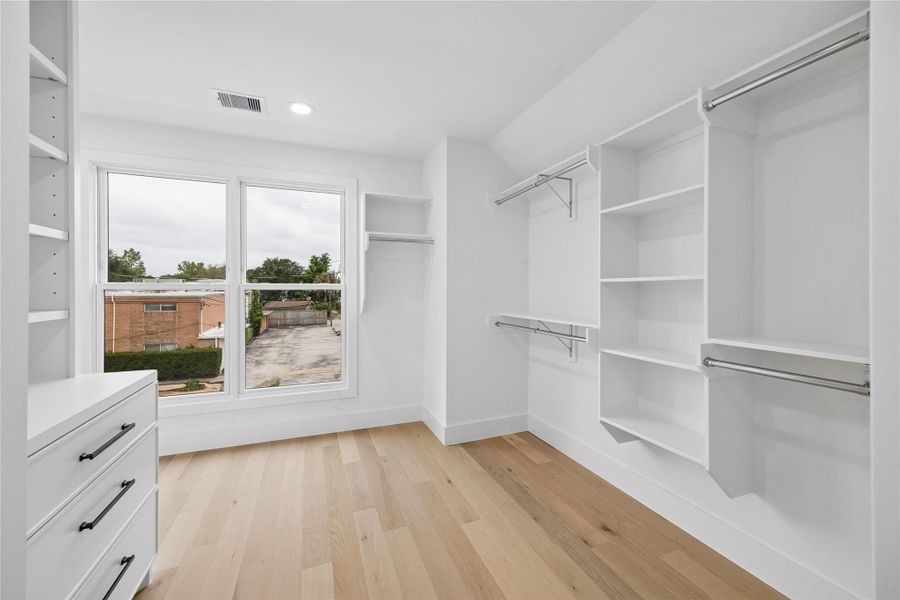 The primary dressing area includes extensive shelving, drawer storage, hanging space, and integrated organization designed to support everyday functionality while maintaining a bright and open feel. Natural light and engineered wood flooring continue the suite’s cohesive design approach into the closet space.