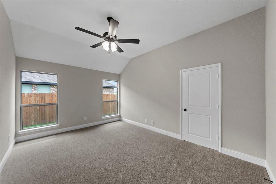 Spacious room featuring vaulted ceilings, a ceiling fan with integrated lighting, neutral-toned walls, and plush carpeting