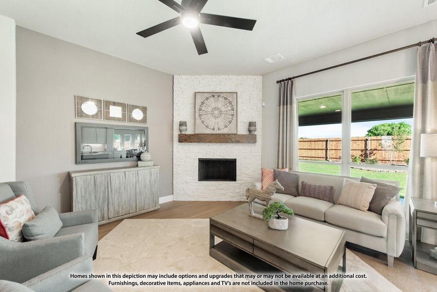 Living room with white brick corner fireplace, ceiling fan, gray sofa, and large window overlooking backyard