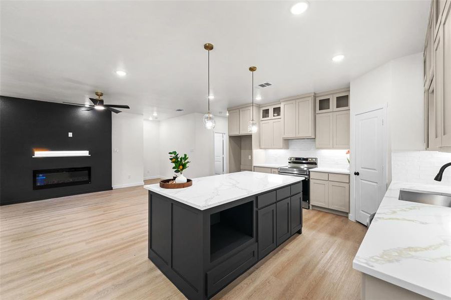 Open-concept living space featuring a central kitchen island with a white countertop, two pendant lights, and light wood-finish flooring throughout Open-concept living space featuring a central kitchen island with a white countertop, two pendant lights, and light wood-finish flooring throughout