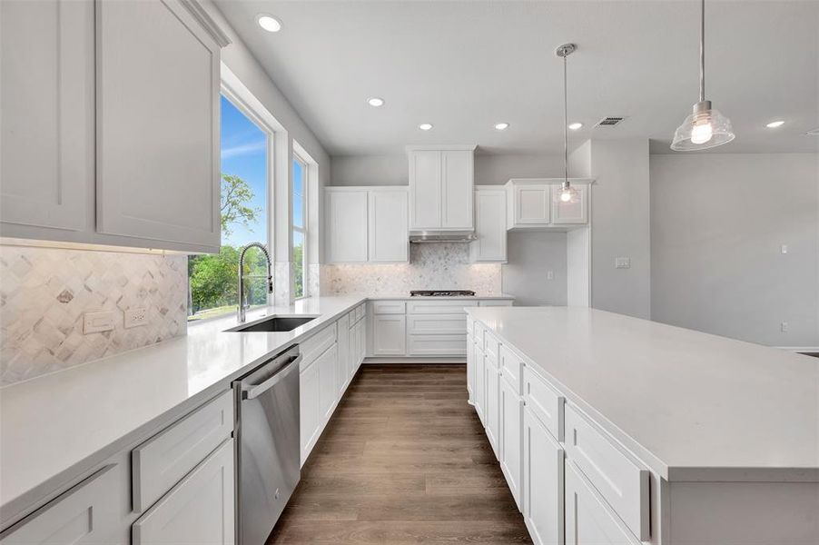 Modern kitchen featuring abundant white cabinetry, white countertops, stainless steel appliances, a decorative tile backsplash, and wood-finish flooring