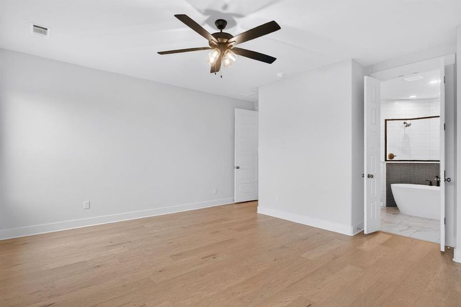 Spacious room featuring wood-finish flooring, a contemporary ceiling fan, and crisp white walls Spacious room featuring wood-finish flooring, a contemporary ceiling fan, and crisp white walls