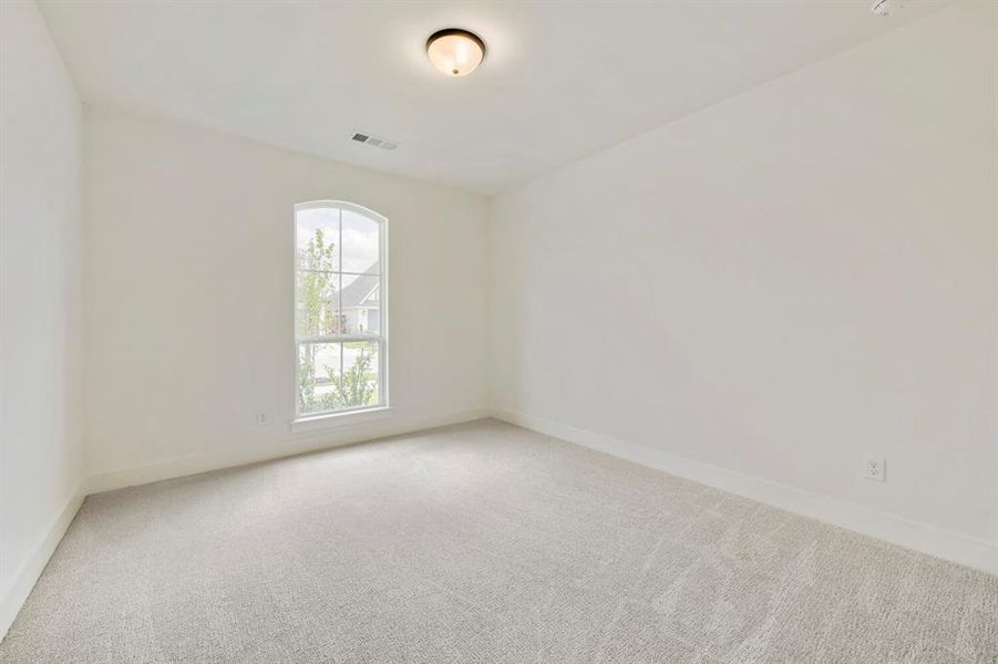Bright interior room featuring a large arched window, light gray carpet flooring, white walls, and a ceiling-mounted light fixture Bright interior room featuring a large arched window, light gray carpet flooring, white walls, and a ceiling-mounted light fixture
