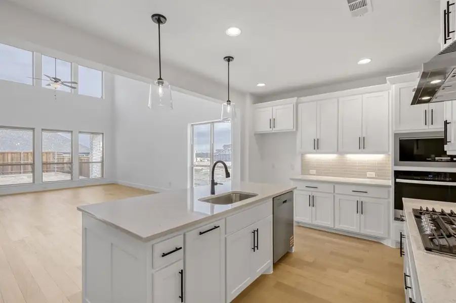 Kitchen with hanging light fixtures, white cabinetry, tasteful backsplash, stainless steel appliances, and light wood finished floors