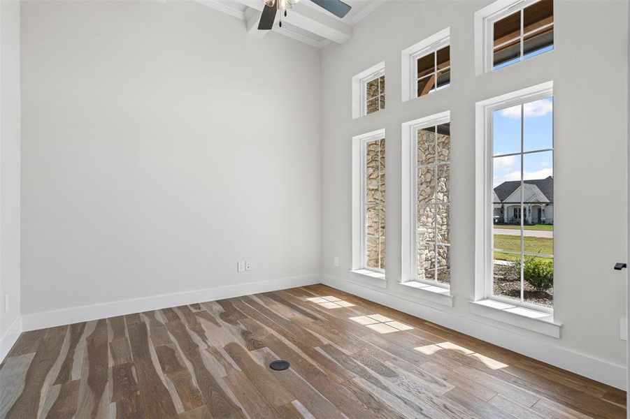 Empty room featuring light wood-type flooring, ornamental molding, a ceiling fan, and beamed ceiling