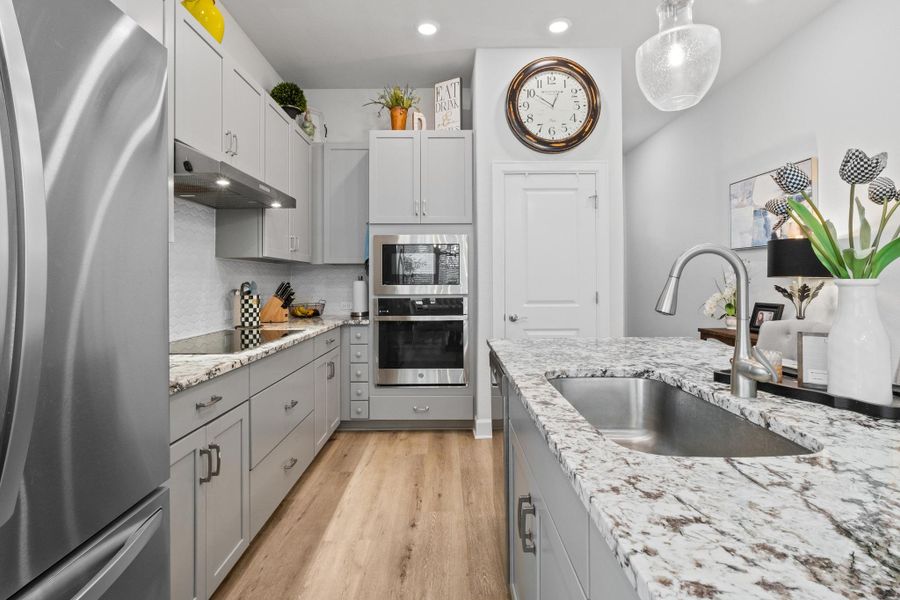 Kitchen featuring appliances with stainless steel finishes, a sink, gray cabinetry, light wood finished floors, and under cabinet range hood Kitchen featuring appliances with stainless steel finishes, a sink, gray cabinetry, light wood finished floors, and under cabinet range hood