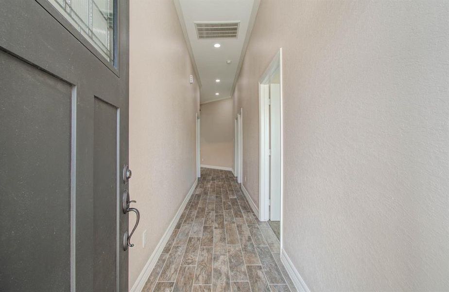 This photo shows a well-lit hallway in a home featuring neutral wall colors, tiled flooring, and multiple doors leading to various rooms.