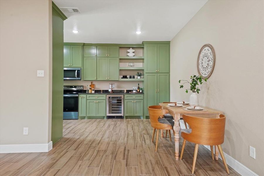Indoor bar featuring green cabinets, open shelves, wood finish floors, wine cooler, and stainless steel appliances Indoor bar featuring green cabinets, open shelves, wood finish floors, wine cooler, and stainless steel appliances