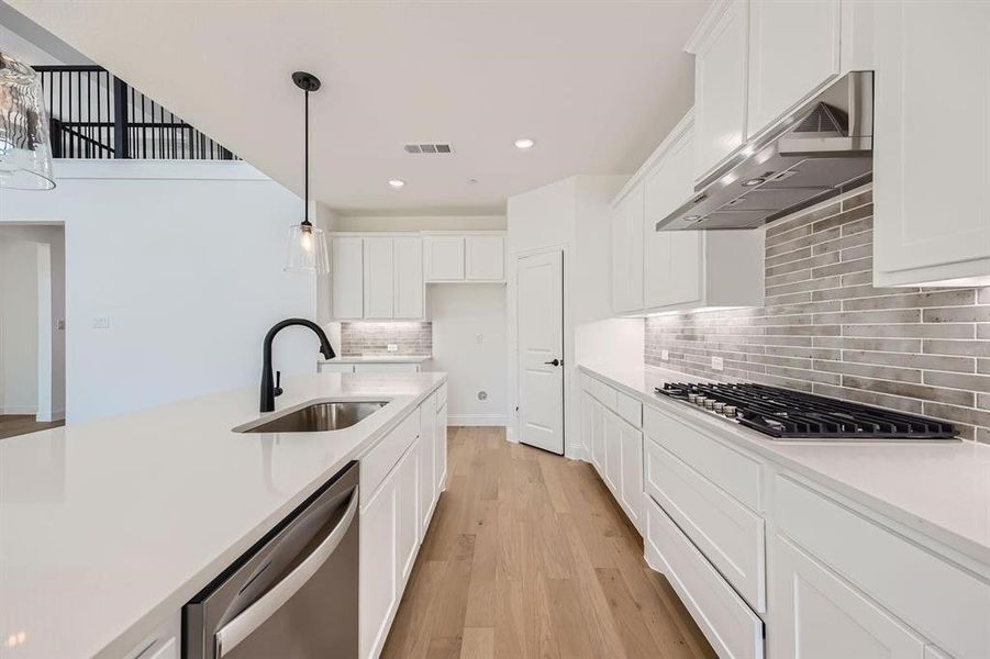 Modern kitchen featuring a large island with an undermount sink and a matte black faucet, stainless steel dishwasher, white cabinetry, and wood-finish flooring Modern kitchen featuring a large island with an undermount sink and a matte black faucet, stainless steel dishwasher, white cabinetry, and wood-finish flooring