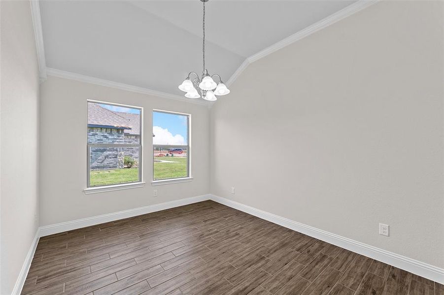 Spare room with ornamental molding, vaulted ceiling, a notable chandelier, and wood-type flooring