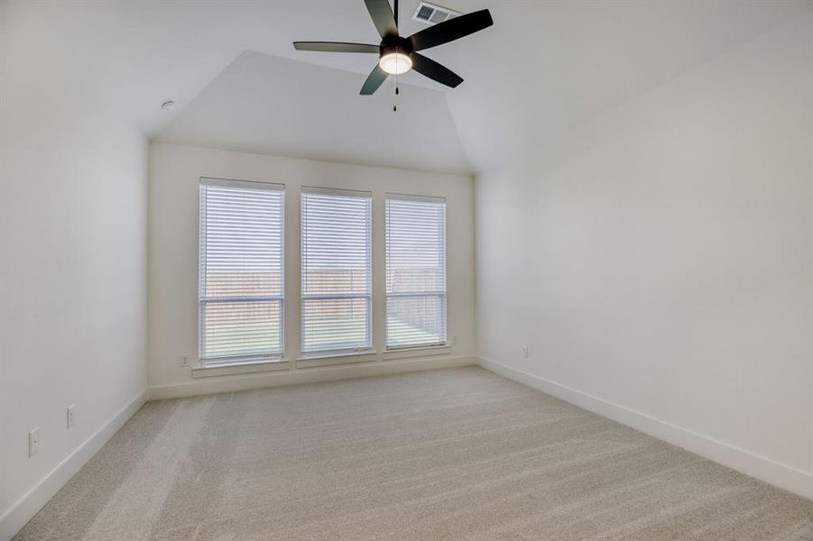 Vaulted ceiling bedroom featuring a contemporary ceiling fan, three windows with horizontal blinds, neutral-toned carpeting, and white baseboards