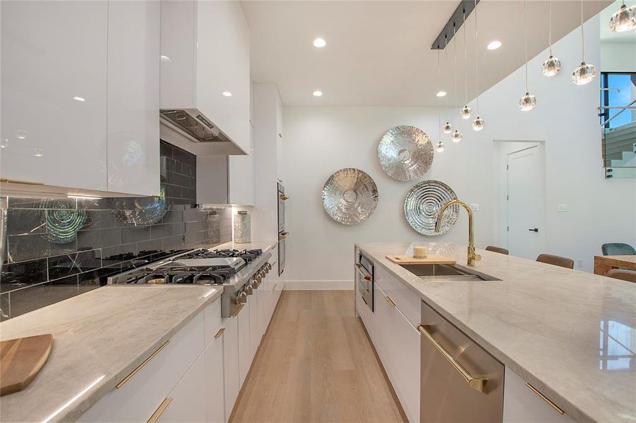 Kitchen featuring pendant lighting, sink, white cabinetry, light hardwood / wood-style flooring, and appliances with stainless steel finishes