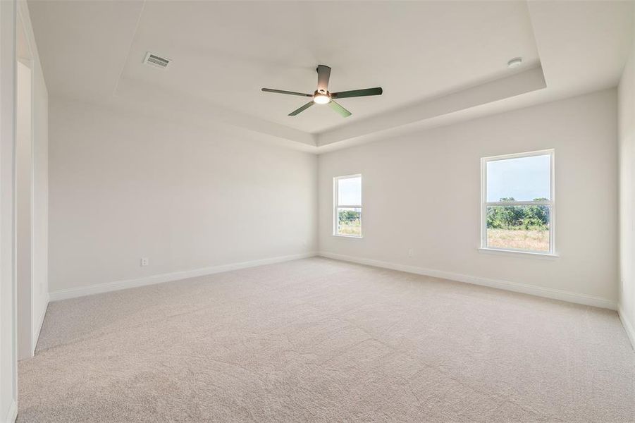 Spare room with a tray ceiling, ceiling fan, light carpet, and a smoke detector