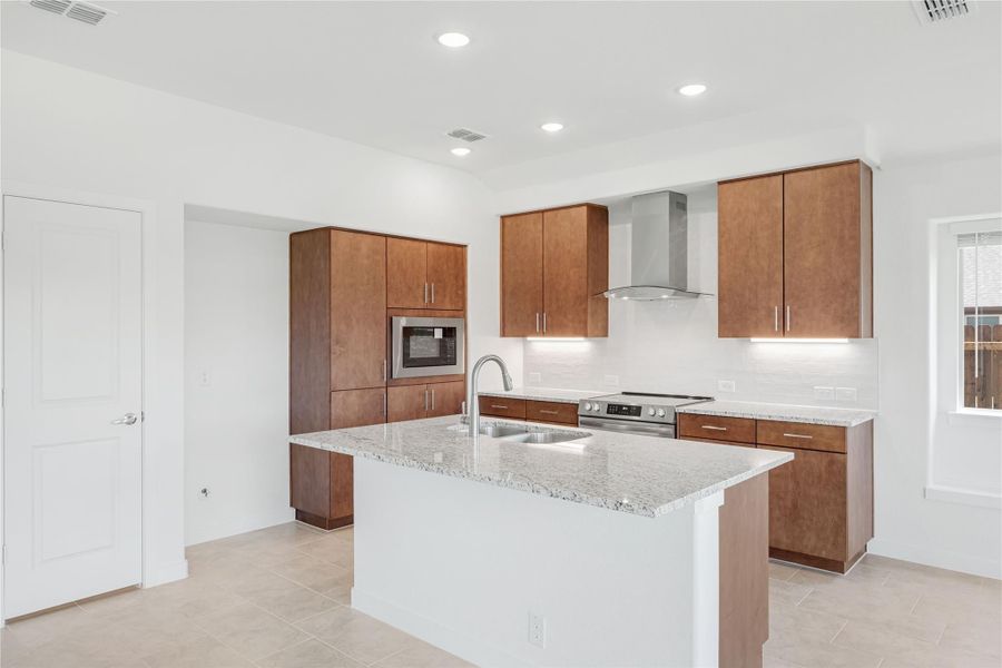 Kitchen with granite island, wood cabinets, stainless steel appliances, and wall-mounted range hood