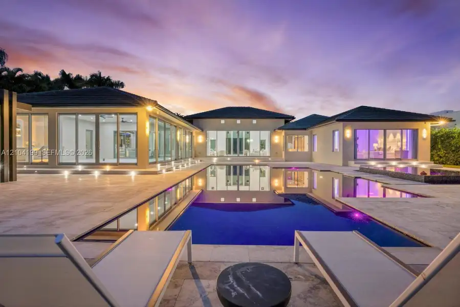 Exterior featuring an expansive stone patio, a multi-section swimming pool with integrated spa, floor-to-ceiling glass wall systems, and low-profile recessed exterior lighting