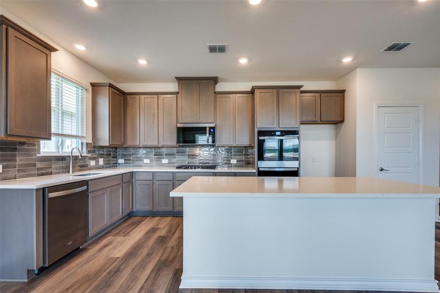 Kitchen featuring dark wood-type flooring, a center island, backsplash, recessed lighting, and stainless steel appliances Kitchen featuring dark wood-type flooring, a center island, backsplash, recessed lighting, and stainless steel appliances